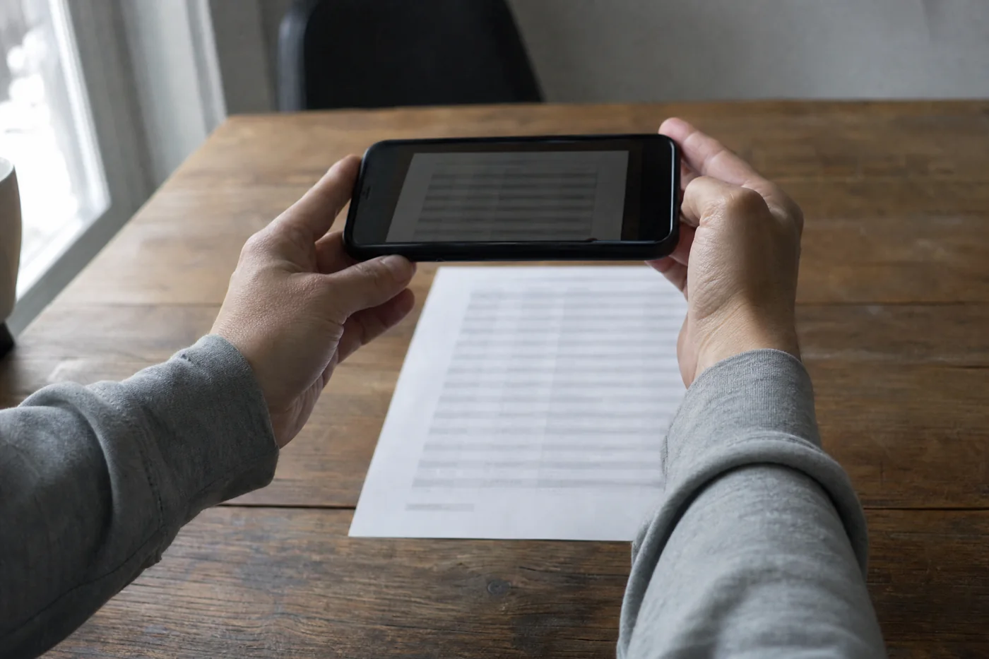 Two hands holding a phone up to photograph a printed lab report on a wooden table.