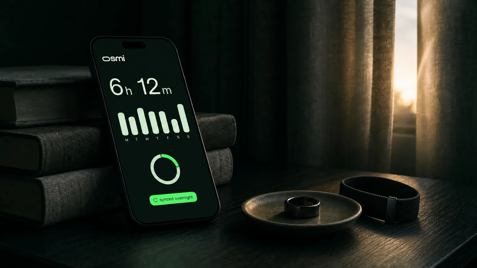 A phone on a bedside table at first light, showing last night's sleep of 6 hours 12 minutes synced overnight, beside a smart ring resting in a small dish.